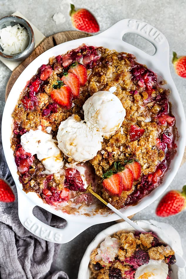 Top view of baked healthy strawberry rhubarb crisp in a white pie pan with coconut ice cream and a spoon