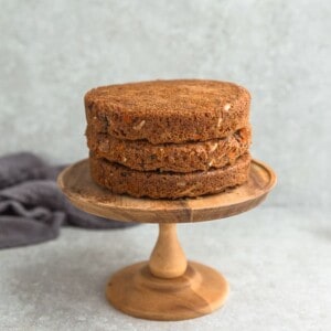Three cooled layers of carrot cake stacked on top of a wooden cake stand
