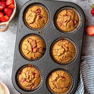 Top view of six strawberry muffins in a muffin pan on a grey background