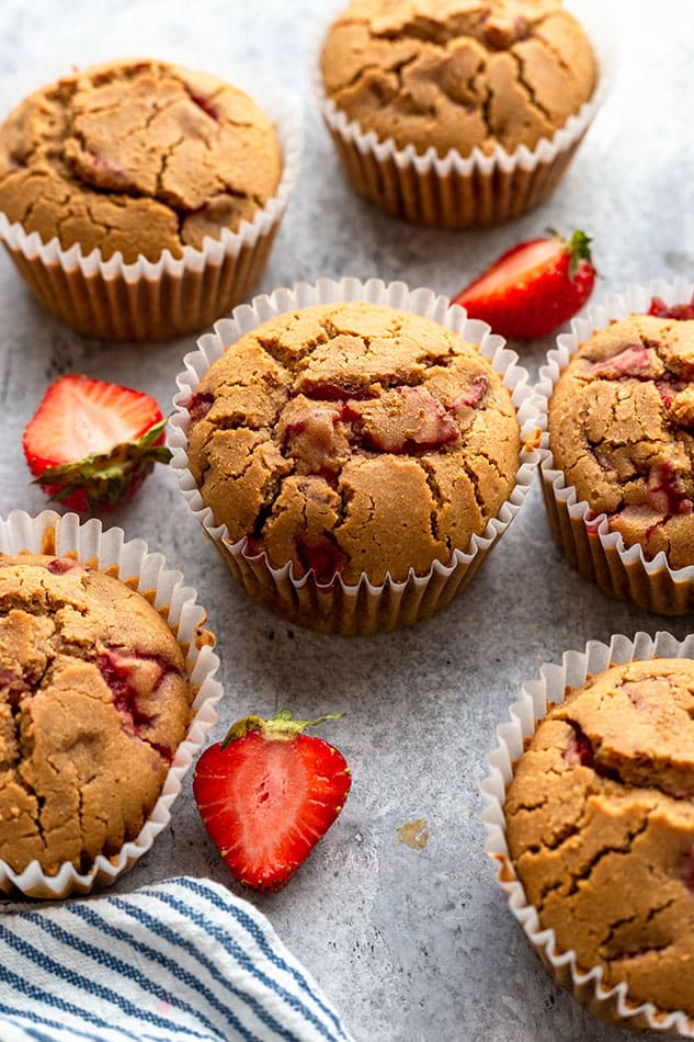 Side view of strawberry muffins on grey surface with fresh strawberries.