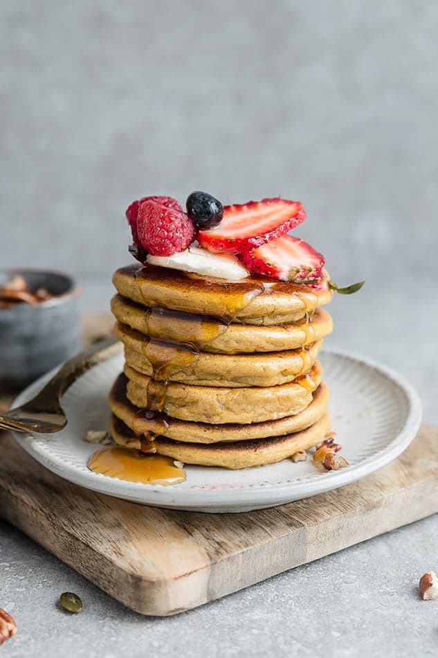 One stack of paleo pancakes on white plate garnished with fresh berries.
