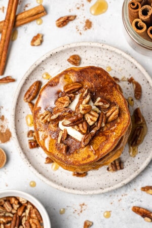 Overhead view of a stack of pumpkin pancakes topped with pecans, butter and maple syrup