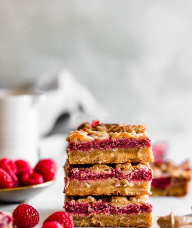 Side view of three raspberry crumb bars stacked on a white background