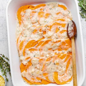 Sliced sweet potatoes in a baking dish topped with cream sauce