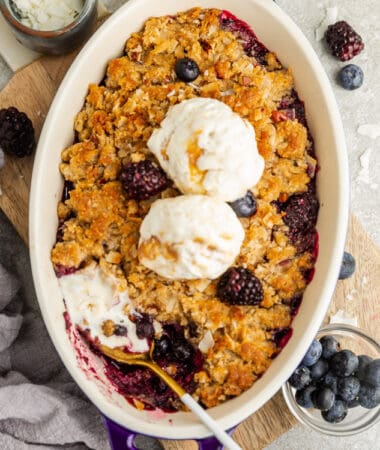 Top view of mixed berry crisp in a blue baking pan with a scoop of dairy free vanilla ice cream and a spoon