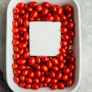 Cherry tomatoes in a white casserole dish with a a block of feta