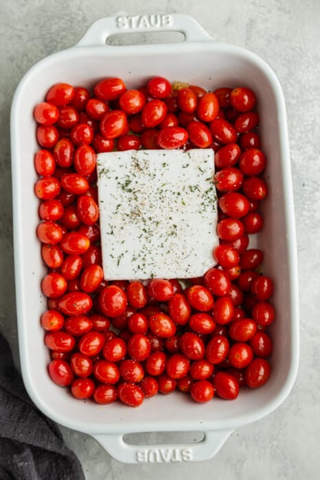 Cherry tomatoes in a white casserole dish with a a block of seasoned feta