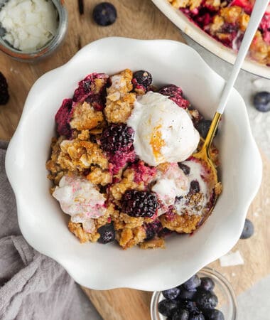 Top view of mixed berry crisp in a white bowl with a scoop of dairy free vanilla ice cream and a spoon