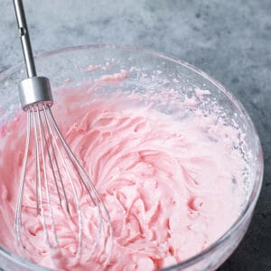 Top view of whipped strawberry milk in a clear bowl with a whisk