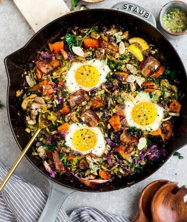 Top view of sweet potato hash with bacon and eggs in a cast-iron skillet on a grey background