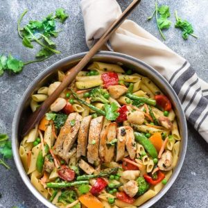 Top view of pasta primavera topped with sliced chicken in a skillet