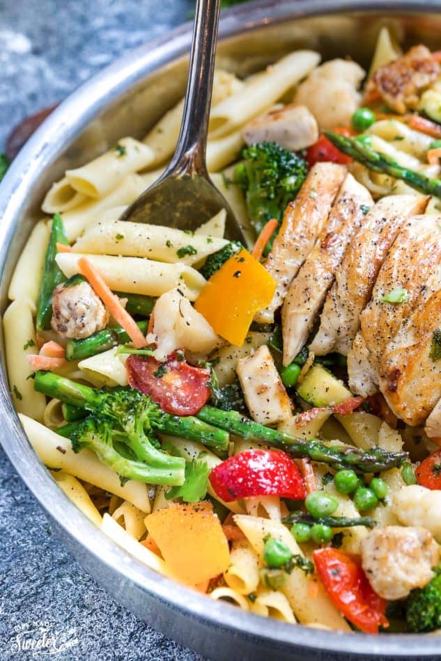 Close-up of pasta primavera topped with sliced chicken in a skillet
