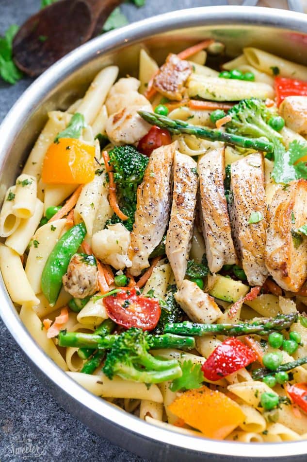 Close-up of pasta primavera topped with sliced chicken in a skillet