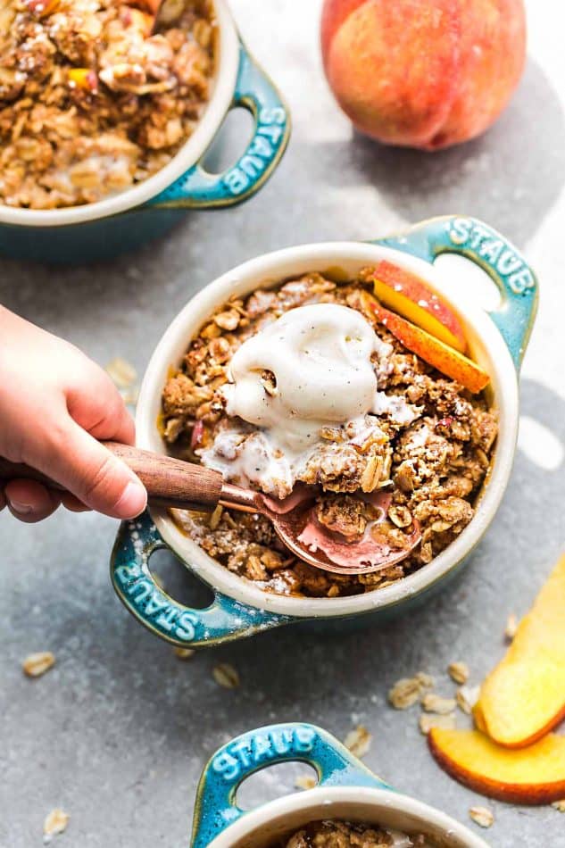 Close-up top view of peach crisp in a blue ramekin with vegan ice cream and a spoon