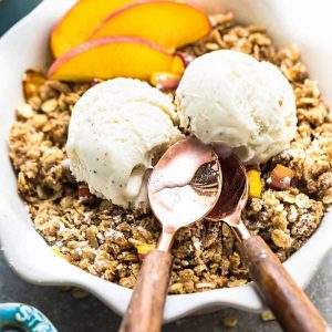 Top view of peach crisp in a white pie pan with vegan ice cream and a spoon