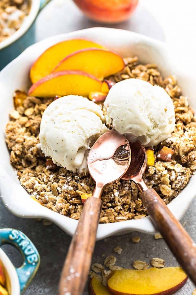 Top view of peach crisp in a white pie pan with vegan ice cream and a spoon