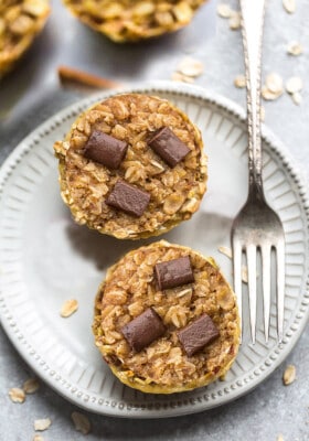 Two portions of peanut butter baked oatmeal cup on a white plate with a fork with three chocolate chunks pressed into the top