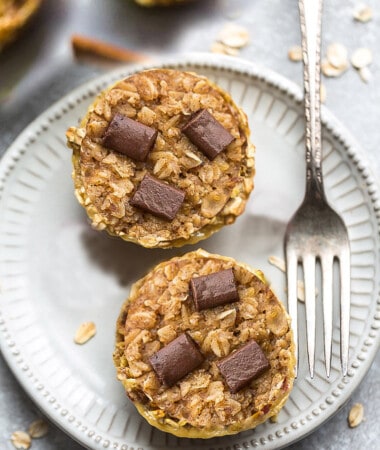 Two portions of peanut butter baked oatmeal cup on a white plate with a fork with three chocolate chunks pressed into the top