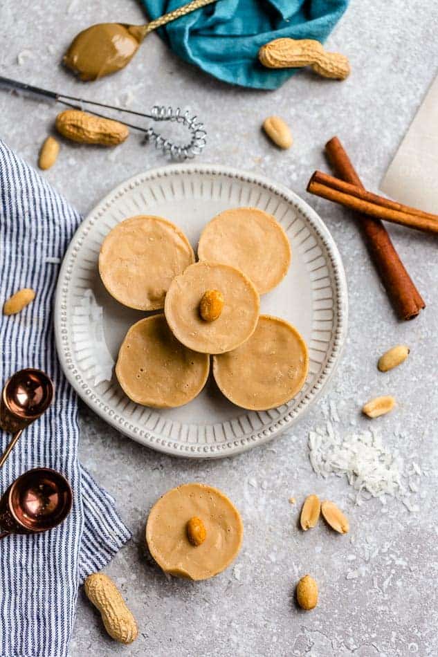 Top view of 5 Peanut Butter Cups on a white plate on a grey board with peanuts and cinnamon sticks