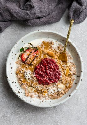 Top view of keto peanut butter oatmeal in a white bowl with strawberry chia seed jam in center with spoon and napkin