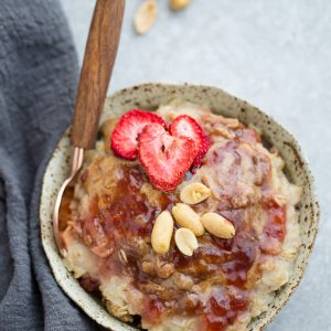 Top view of a bowl of Peanut Butter and Jelly Oatmeal on a grey background with a spoon