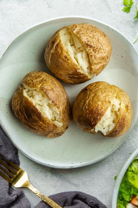 Three air fryer baked potatoes on a white plate