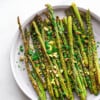 Overhead shot of a batch of air fryer asparagus topped with pistachios on a white plate