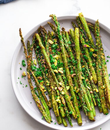 Overhead shot of a batch of air fryer asparagus topped with pistachios on a white plate