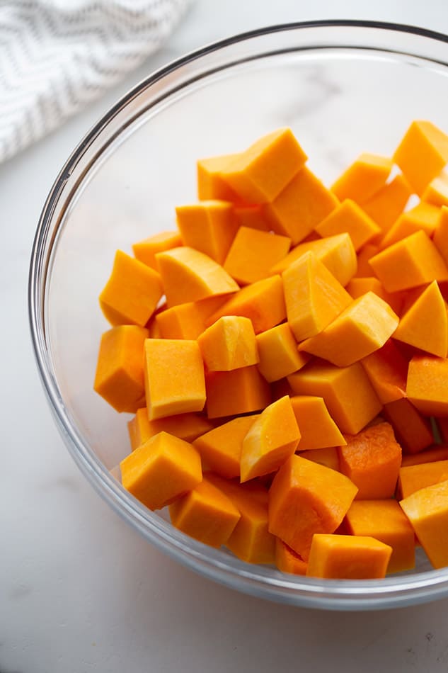 Cubes of raw butternut squash inside of a large glass mixing bowl