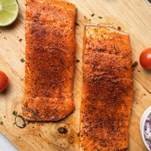Two raw seasoned salmon fillets on a wooden cutting board
