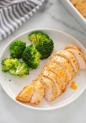Overhead view of one serving of oven baked chicken breast sliced with a side of steamed broccoli on a white plate