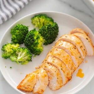 Overhead view of one serving of oven baked chicken breast sliced with a side of steamed broccoli on a white plate