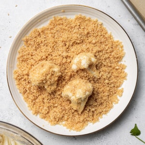 Three cauliflower florets in a plate of crushed crackers