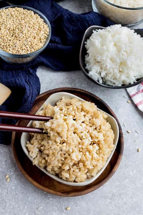 A Bowl of Fluffy Brown Rice with Two Chopsticks Picking Up a Bite