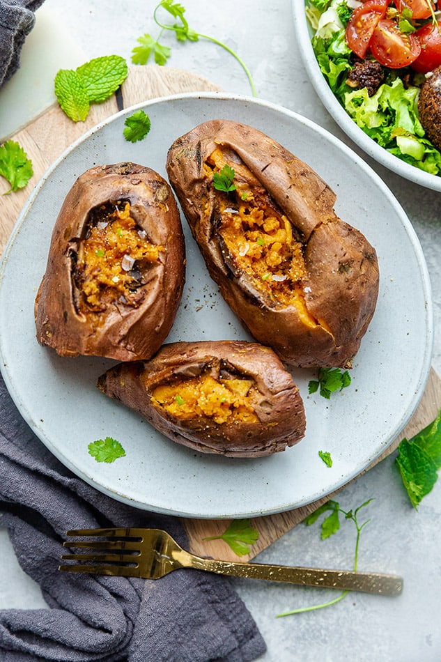 Three Instant Pot baked sweet potatoes with parsley on a white plate