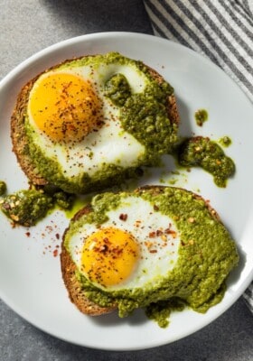 Two fried pesto eggs served over toast and pesto on a white plate