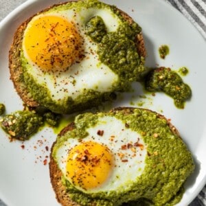 Two fried pesto eggs served over toast and pesto on a white plate