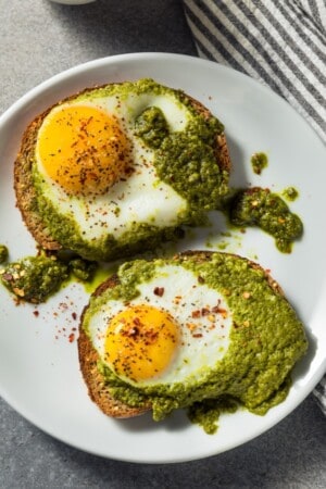 Two fried pesto eggs served over toast and pesto on a white plate
