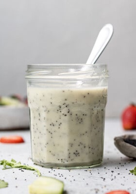 Side view of poppy seed dressing in a small jar with a spoon