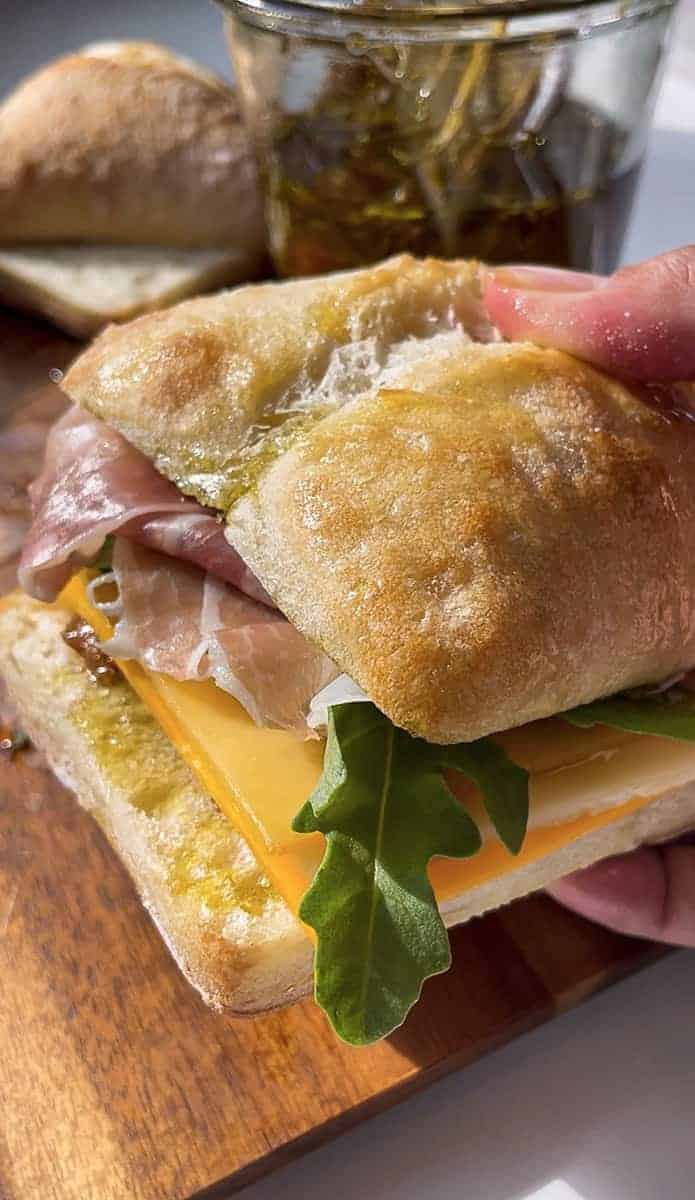 A hand holding a Prosciutto sandwich with prosciutto, arugula and cheese