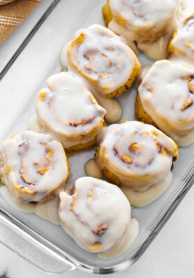 Top view of frosted dairy free pumpkin cinnamon roll dough in a clear casserole dish