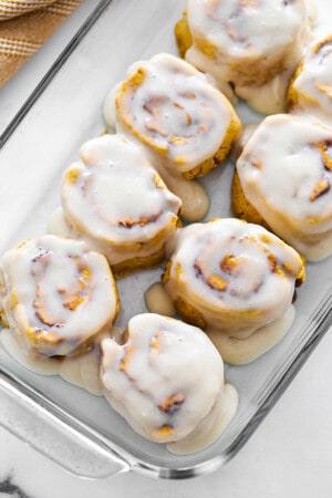 Top view of frosted dairy free pumpkin cinnamon roll dough in a clear casserole dish
