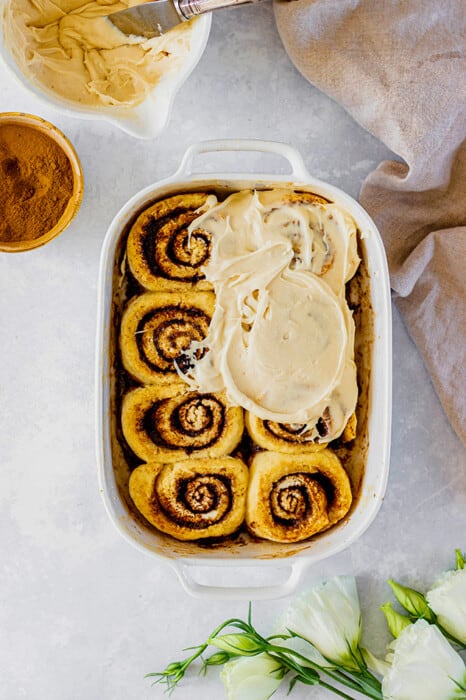 Top view of half frosted gluten free pumpkin cinnamon roll dough in a white baking dish