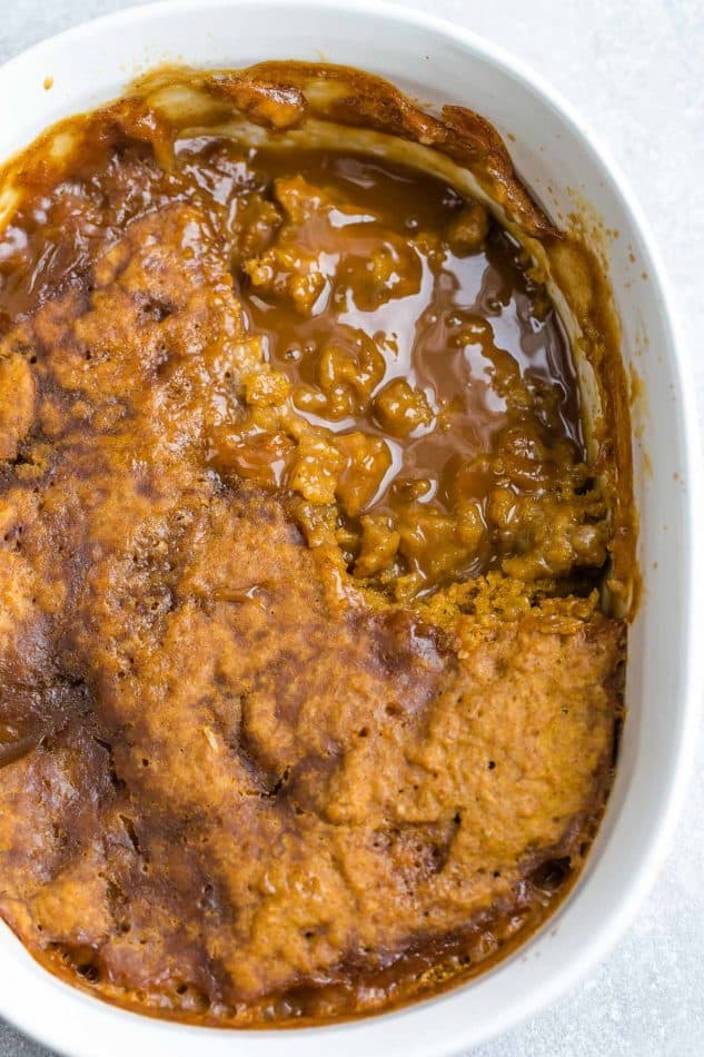 An entire baked pumpkin cake in a white casserole dish with a spoon