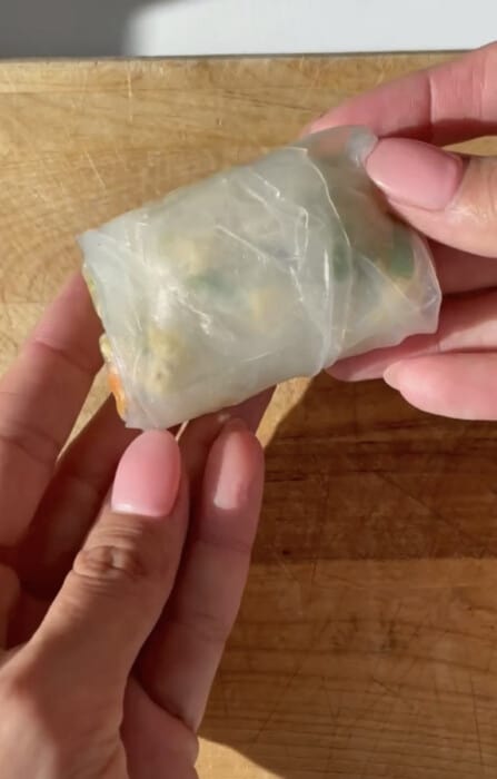Hands holding a wrapped paper dumpling on a wooden cutting board