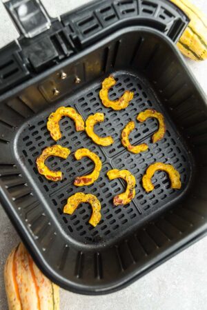 Top view of cooked delicata squash cut into half rings in an air fryer basked