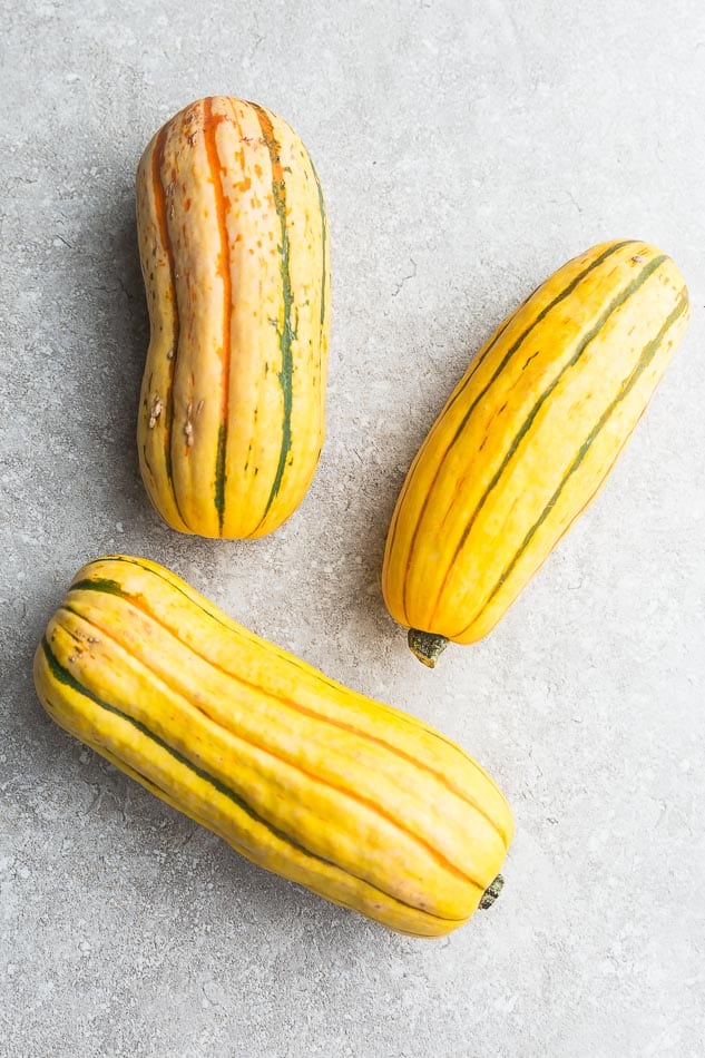 Top view of 3 whole delicata squash on a grey background