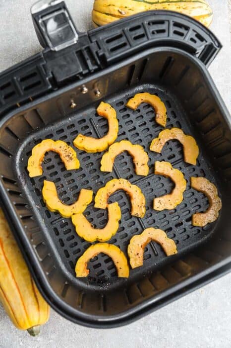 Top view of raw delicata squash cut into half rings in an air fryer basked