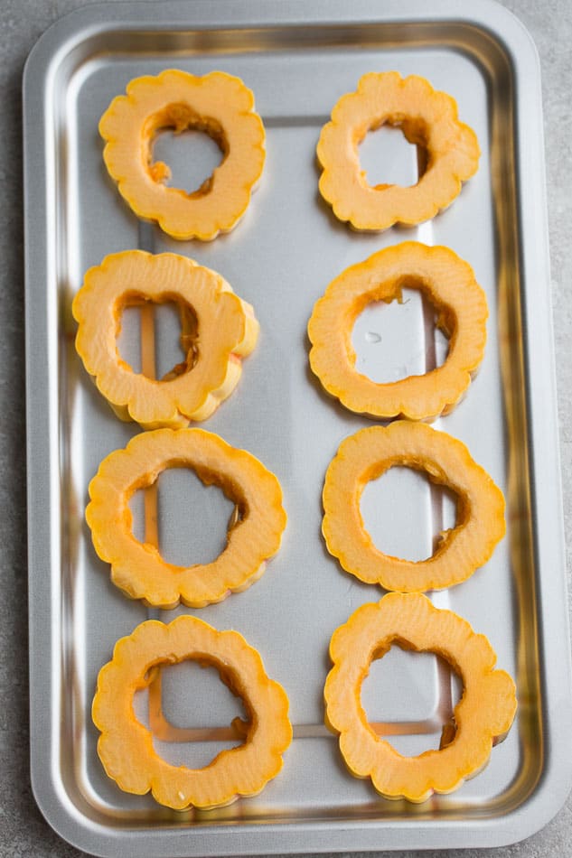 Uncooked delicata cut into rings on a baking sheet