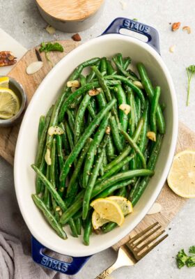 Top view of roasted green beans with garlic in a oval blue casserole dish on a wooden cutting board